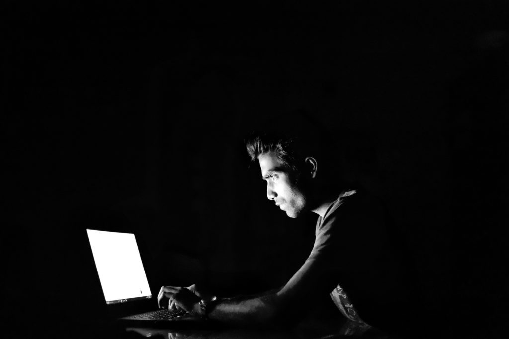 a man using a VPN while on his laptop, sitting in the dark